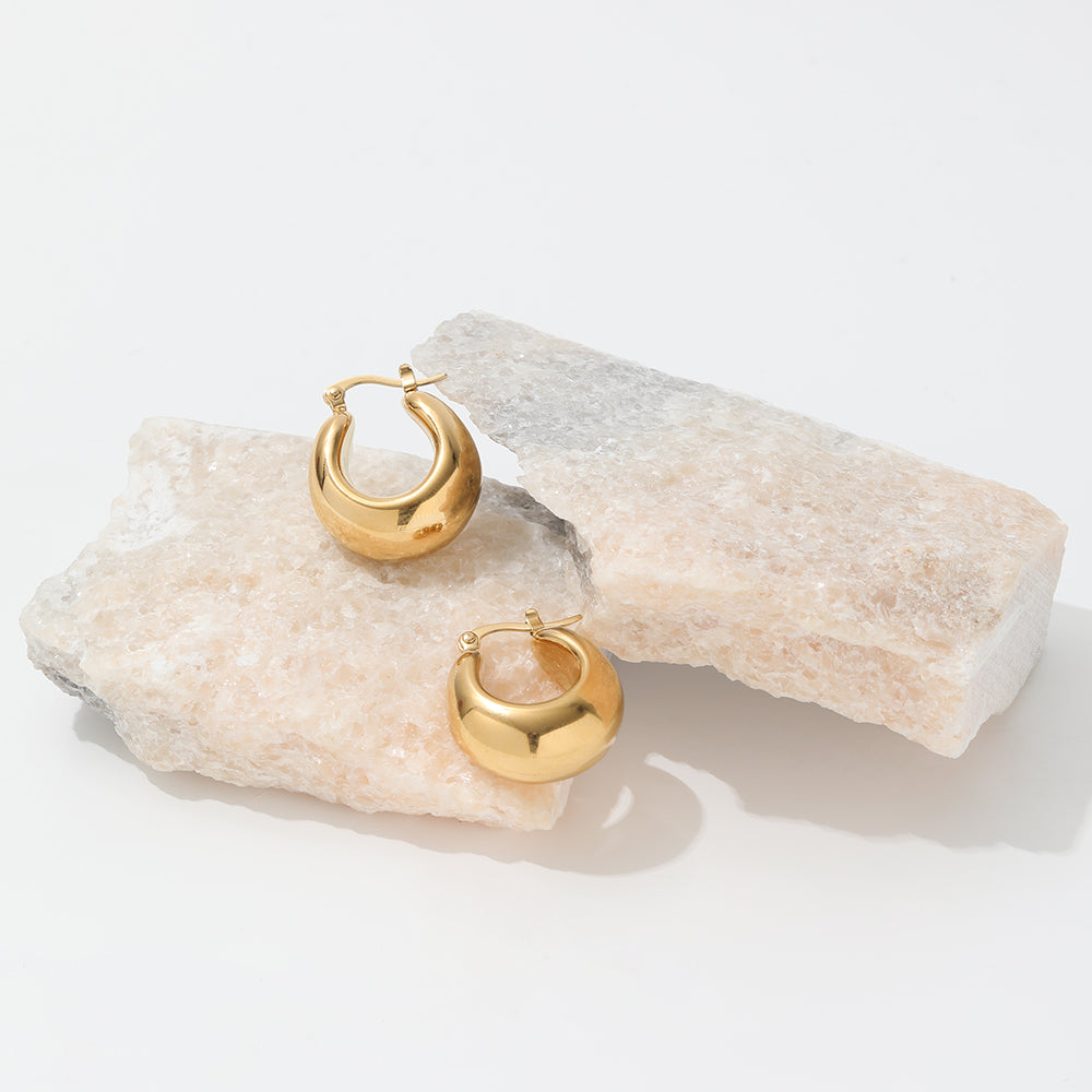 chunky gold hoop earrings on a grey slate