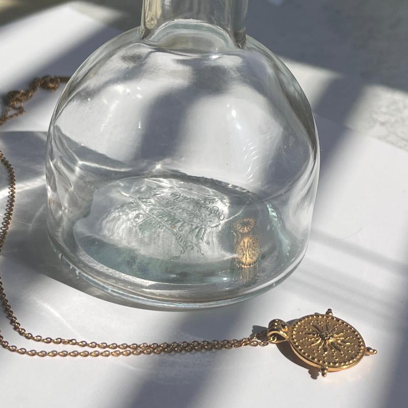 gold daisy ring on top of glass bottle with sun pendant necklace lying beside